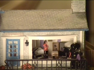 den has two tables, a lamp, a big screen TV, stereo speakers, and a 