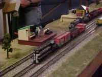 A close-up view of a NYC switch train, an RS3 switch engine with the rocket launcher car in tow, the saw mill and Barrel loader accessories.