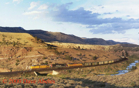 A UP westbound loaded coal train pounds upgrade between Kyune and Colton, UT with helpers just out of view around the corner; 08/19/00